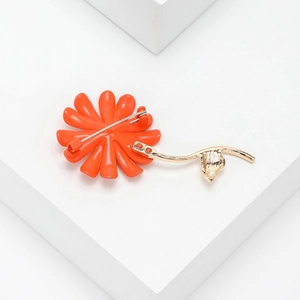 Detailed view of orange daisy brooch with golden stem on white geometric background