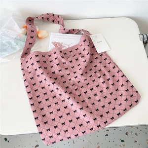 Detail of pink canvas tote bag with black bow pattern and brand tag on desk