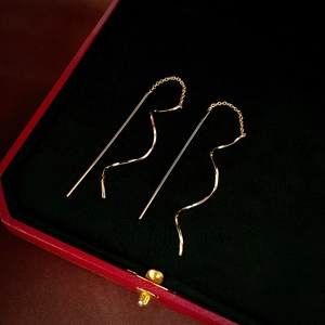 Detail of golden wave chain tassel earrings on a black velvet jewelry box tray