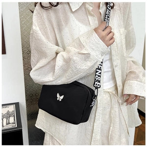 Detail of black nylon crossbody bag with butterfly ornament and lettered wide strap