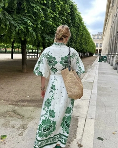Back view of a white floral maxi dress with lantern sleeves and a straw bag in a garden