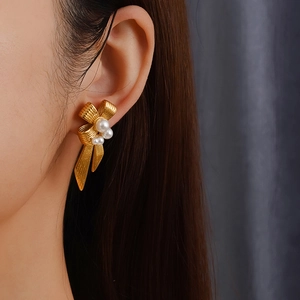 Chic golden bow earrings with white pearls shown on a model for a trendy fashion look