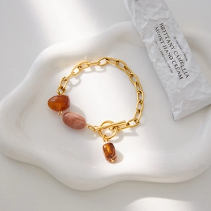 Golden chain bracelet with amber resin stones and T-bar clasp on a ceramic stand