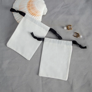 Close-up of two off-white cotton jewelry pouches with black ribbons and pearl earrings