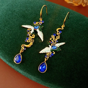 Macro view of vintage gold crane earrings with blue gems on green velvet fabric