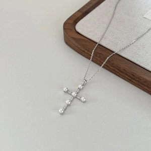 Detailed view of silver cross pendant with white pearls and small diamonds on thin chain