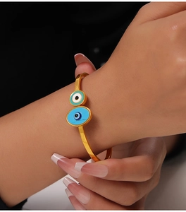 Detail of bohemian gold titanium steel cuff bracelet with blue evil eye enamel charms
