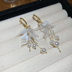 Detailed view of gold petal earrings with acrylic resin and white pearl tassels