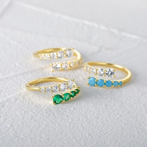 Detail of three adjustable gold rings with white, emerald green, and turquoise gemstones