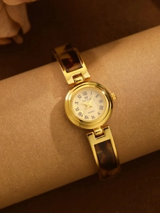Detail of elegant gold-tone chain watch with amber tortoise shell links and Roman numerals