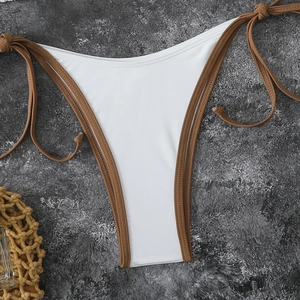 Detail view of white and brown tie-side bikini bottom on a textured stone surface