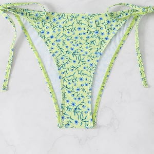 Detail of light green floral bikini bottoms with adjustable side-tie design on marble