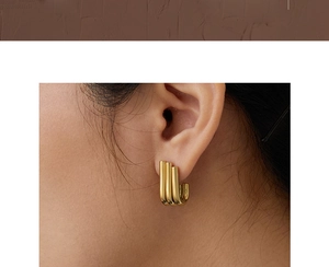 Close-up of elegant triple gold tubes J-shaped polished earrings worn by a model