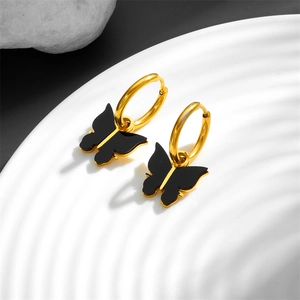 Minimalist gold hoop earrings with black butterfly charms on a white textured display