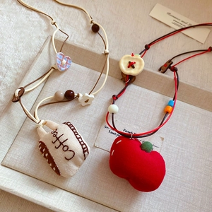 Detail of handmade fabric necklaces with embroidered coffee cup and red apple pendants