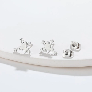 Minimalist silver frog stud earrings shown on a white stone display platform