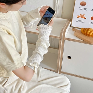 Close-up of white knitted arm warmer with delicate bow detail and wavy scalloped edges