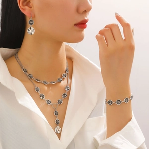 Close-up of layered silver necklace and earrings set with smoky grey square stones