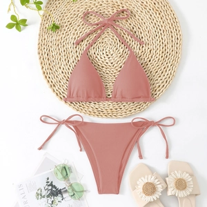 Flat lay of pink ribbed triangle bikini with neck tie and side-tie bottoms on straw mat
