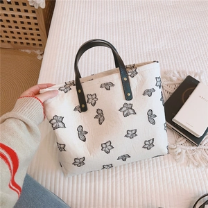 Détail du sac cabas en toile avec broderie noire et anses en cuir à rivets dorés