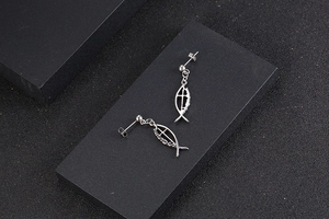 Detail shot of silver hollow ichthys fish earrings with cross design on black platform