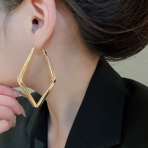 Close-up of a large golden geometric diamond-shaped metal earring worn by a model