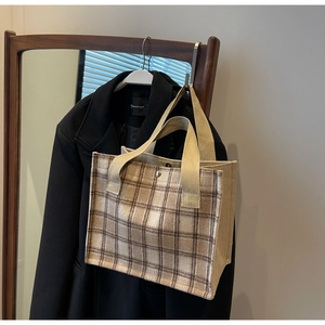 Detail of a beige and brown plaid canvas tote bag hanging on a wooden hanger with snap button