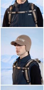 Detail of a brown knitted winter hat with ear flaps and peak in a snowy outdoor setting