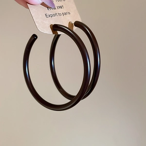 Detail of large brown acrylic round stud earrings on a card held by hand