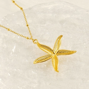 Elegant gold starfish pendant necklace made of stainless steel on a textured glass plate