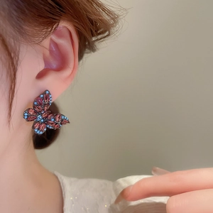 Vintage butterfly stud earrings with red gems and blue beads on a model's ear