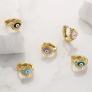 Gold-plated evil eye huggie earrings in five vibrant colors on white marble surface