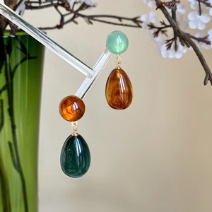Macro shot of resin teardrop earrings in green and amber on a decorative floral display