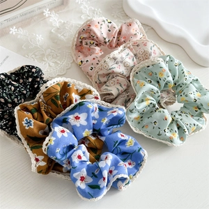 Detailed flat lay of floral fabric hair scrunchies with delicate lace trim in five colors