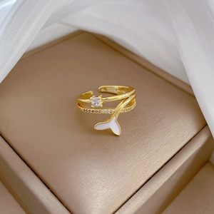 Detail of adjustable gold mermaid tail ring with zircon and white enamel on a stand