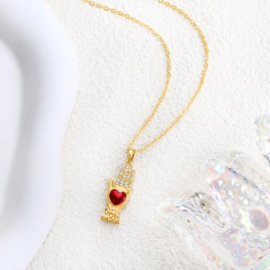 Detail of gold necklace featuring a hand holding a red heart pendant with white zircons