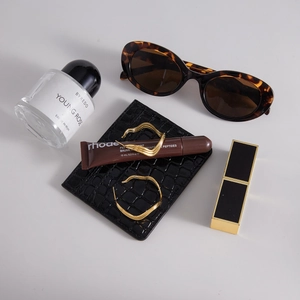 Flat lay of gold wave hoop earrings with sunglasses and cosmetic accessories on a dark pouch