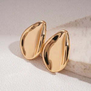 Close-up of golden teardrop leaf earrings with polished finish on marble surface