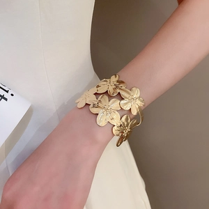 Macro detail of golden flower cuff bracelet featuring textured metal petals and satin finish