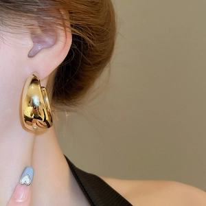 Close-up of model wearing thick gold C-shaped hoop earrings with a glossy mirror finish