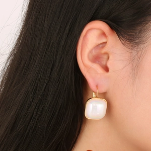 Gros plan d'élégantes boucles d'oreilles carrées en perles dorées portées à l'oreille