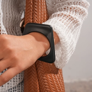 Close-up of matte black acrylic square cuff bracelet worn with a knit top and woven bag