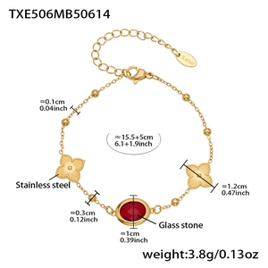 Detalle de pulsera de cuentas de acero inoxidable dorado con piedra roja y tréboles
