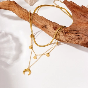 Detail of layered gold snake chain necklace with crescent moon and disc charms on wood