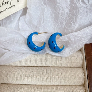 Detailed shot of C-shaped blue enamel earrings with red dots on soft textured paper