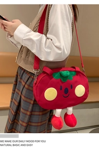 Detailed view of red strawberry plush crossbody bag with cute face on a beige outfit