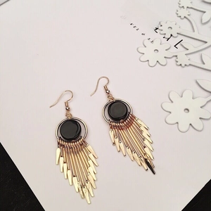 Close-up of golden tassel earrings with black circular studs and metal leaf pendants