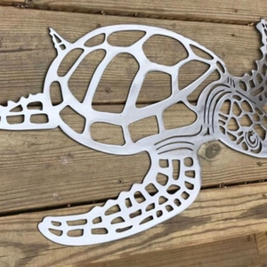 Silver metal sea turtle wall art with intricate cutout design on a wooden deck