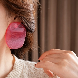Close-up of model wearing oversized pink acrylic earring with matte texture and irregular shape