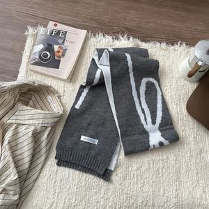 Flat lay of a grey knit scarf with white patterns, magazine and coffee pot on white fur